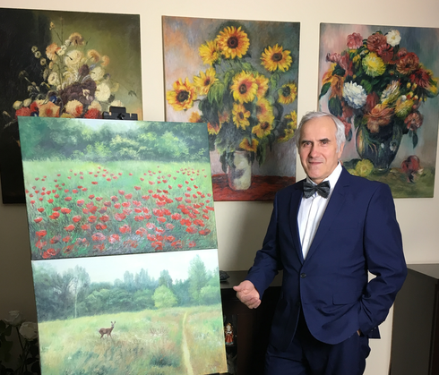 Stanisław Rakowski w granatowym garniturze obok swoich obrazów olejnych: pola maków i łąki z sarną, w tle martwe natury z kwiatami